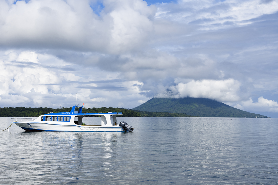 Dive boat on a mooring out front of Siladen Resort & Spa with Bunaken Island and Manado Tua Island in the background.